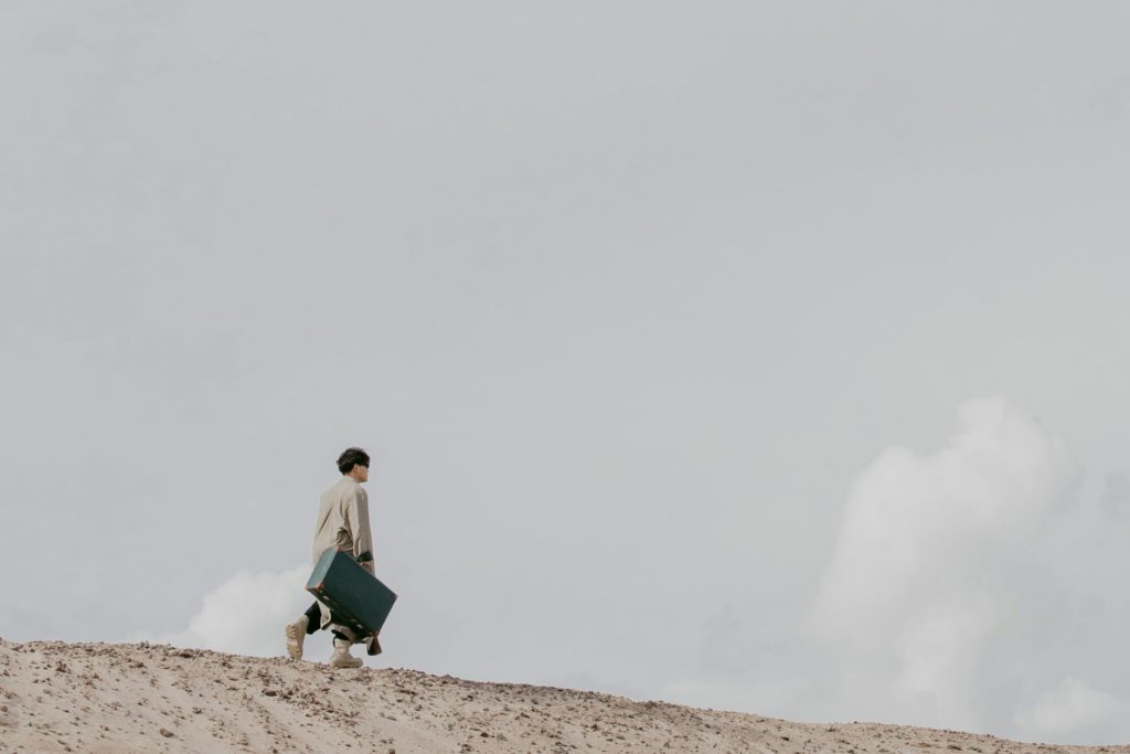 man walking on a desert land with a luggage